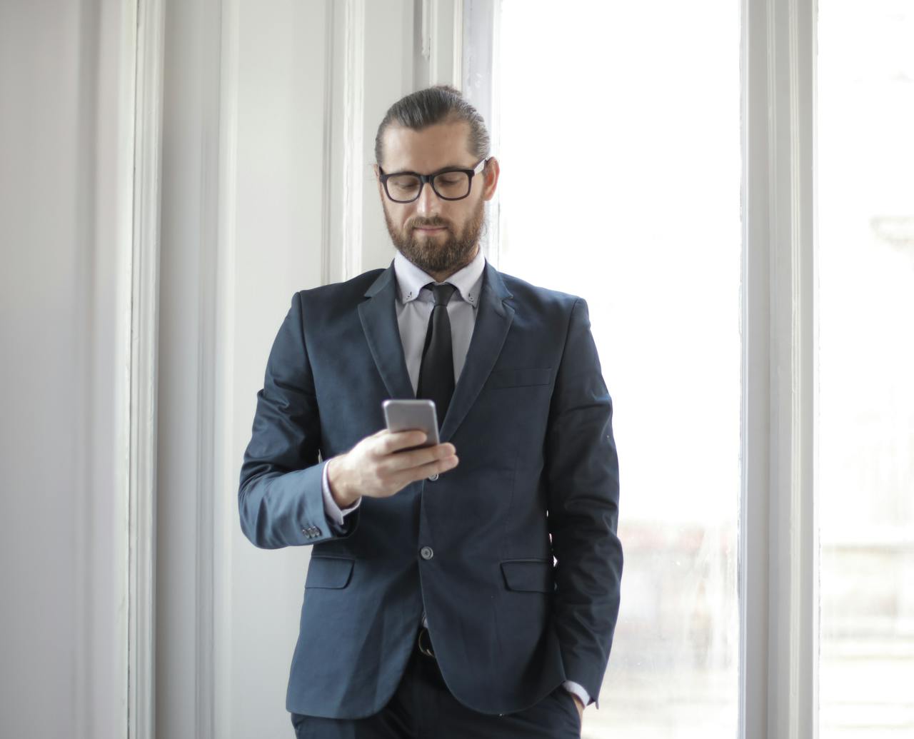 Services Confident man in formal suit using smartphone by window in office setting.