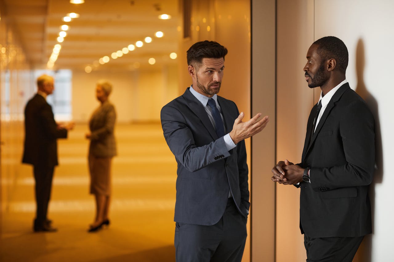 About Two businessmen in formal attire engaged in a serious discussion in a modern office hallway.